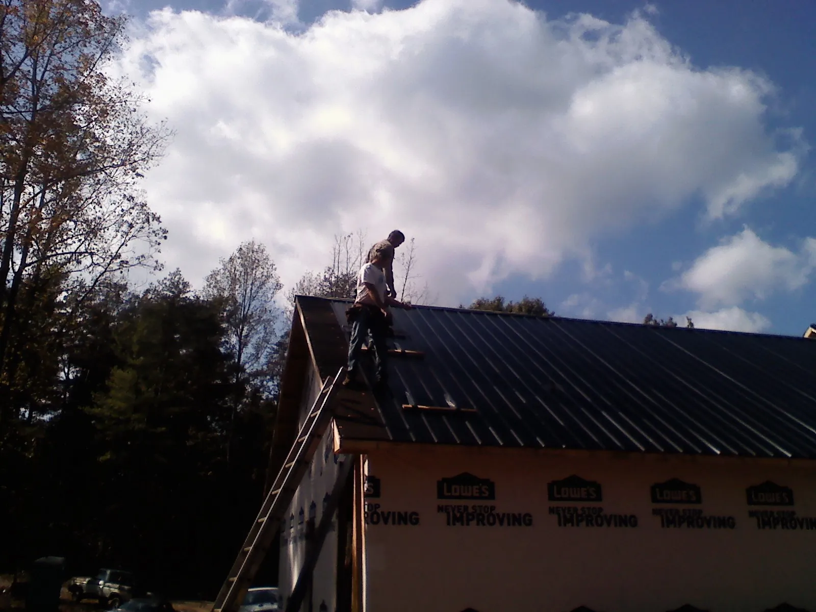 Roofer fastening dark metal panels high against a cloudy sky, from a Roof Inspection job in Dixon