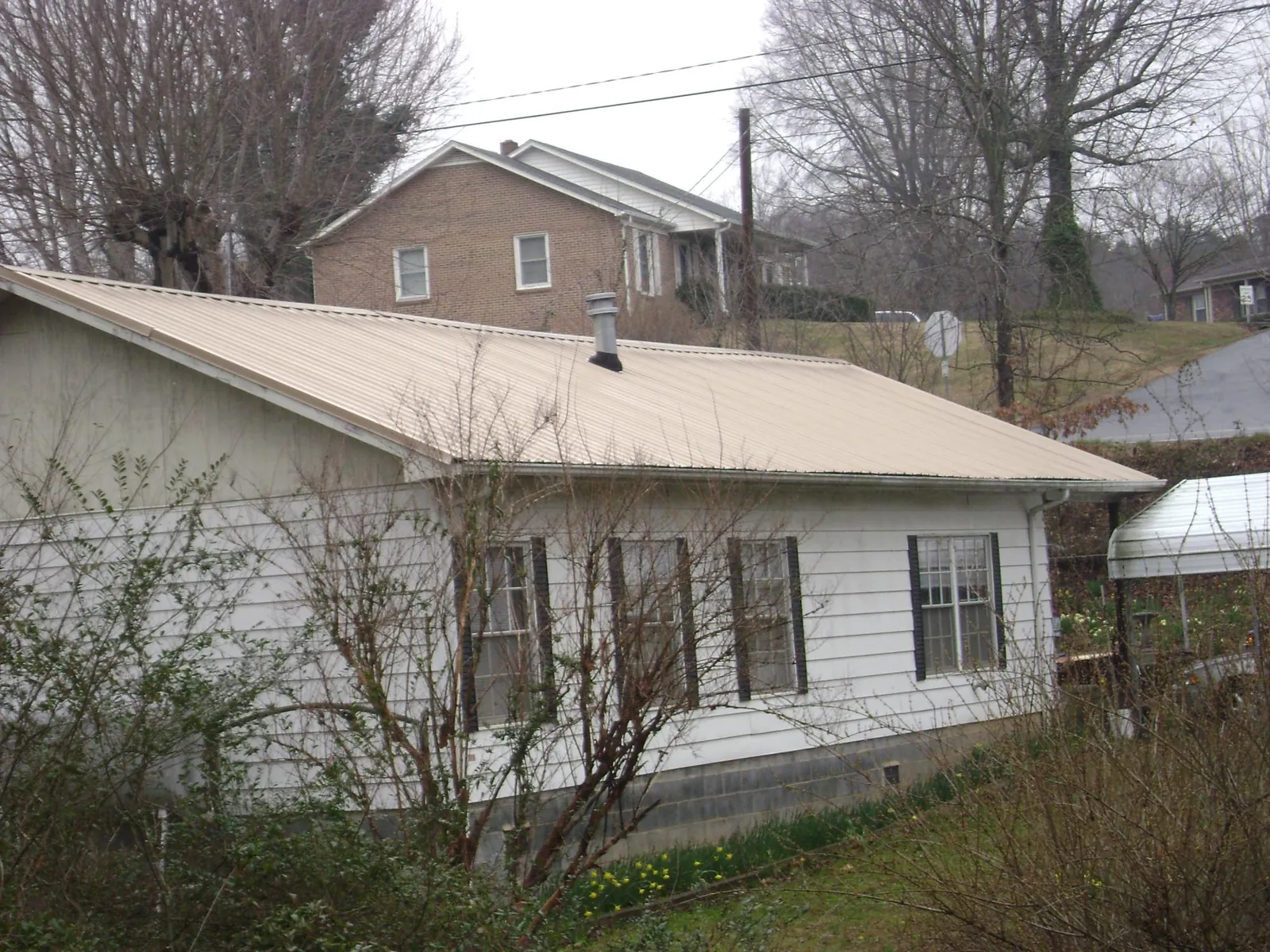 Tan metal roof on a white sided house set into a hillside — Commercial Roofing by Roofing Brothers in Dixon